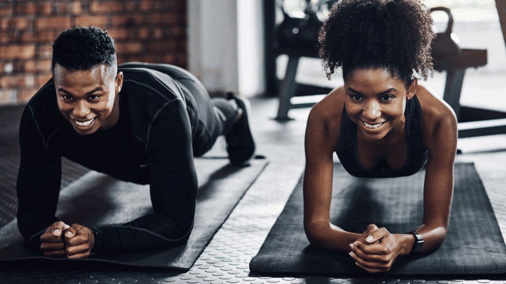 Shot of a young man and woman doing plank exercises together in a gym