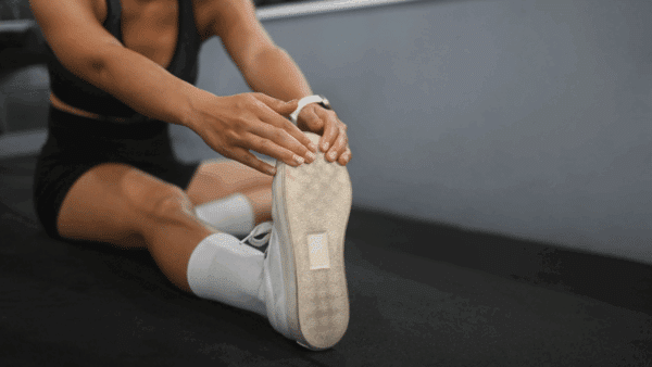 Young sporty woman sitting and stretching her legs after working out in the gym